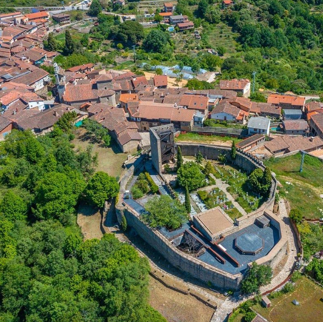 Aerial view of the village with tiled roofs, greenery and a large walled building in the foreground.
