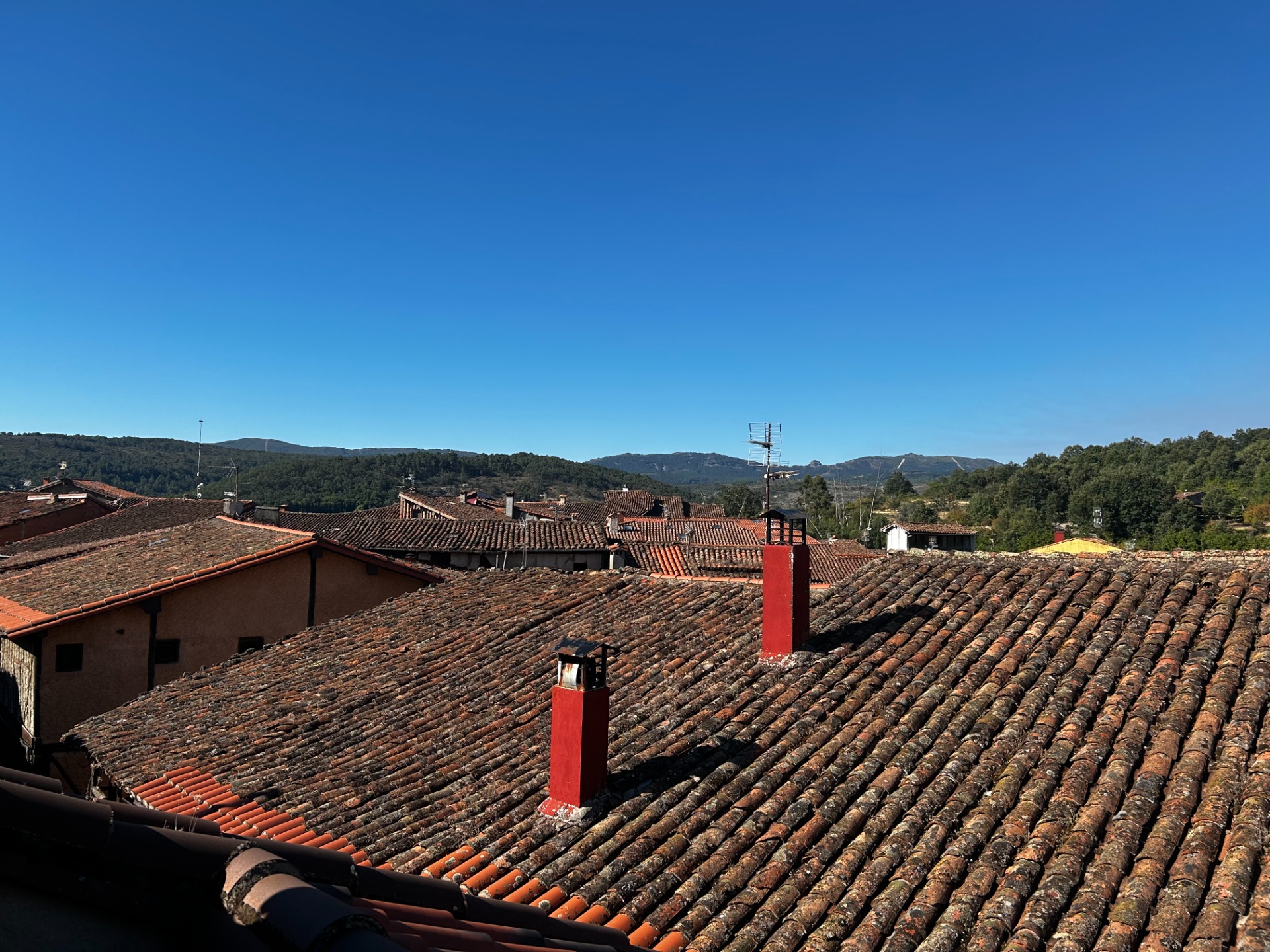 Tejados de teja roja y marrón paisaje montañoso y cielo azul despejado.